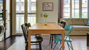 A dining area with a wooden table, black and turquoise chairs, a vase with greenery, and a bicycle artwork on the wall.