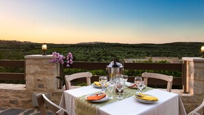 Une table dressée pour deux personnes, avec une bouteille de vin, des verres et des assiettes, donnant sur un vignoble.