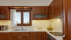 Une cuisine avec des meubles de rangement en bois, un évier, un grille-pain, une cuisinière et une fenêtre ornée d’un rideau blanc.