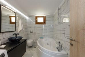 A modern bathroom with a large bathtub, a glass sink, and a toilet.