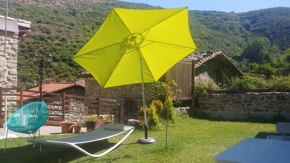 A garden with a yellow umbrella, a stone wall, and a wooden building.