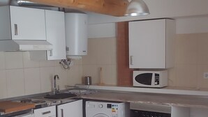 Cocina compacta con electrodomésticos blancos, lavadora y comedor con mesa de vidrio y dos sillas.