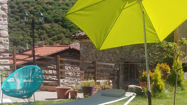Un espacio al aire libre con césped, una sombrilla amarilla, una silla azul y un edificio de piedra al fondo.