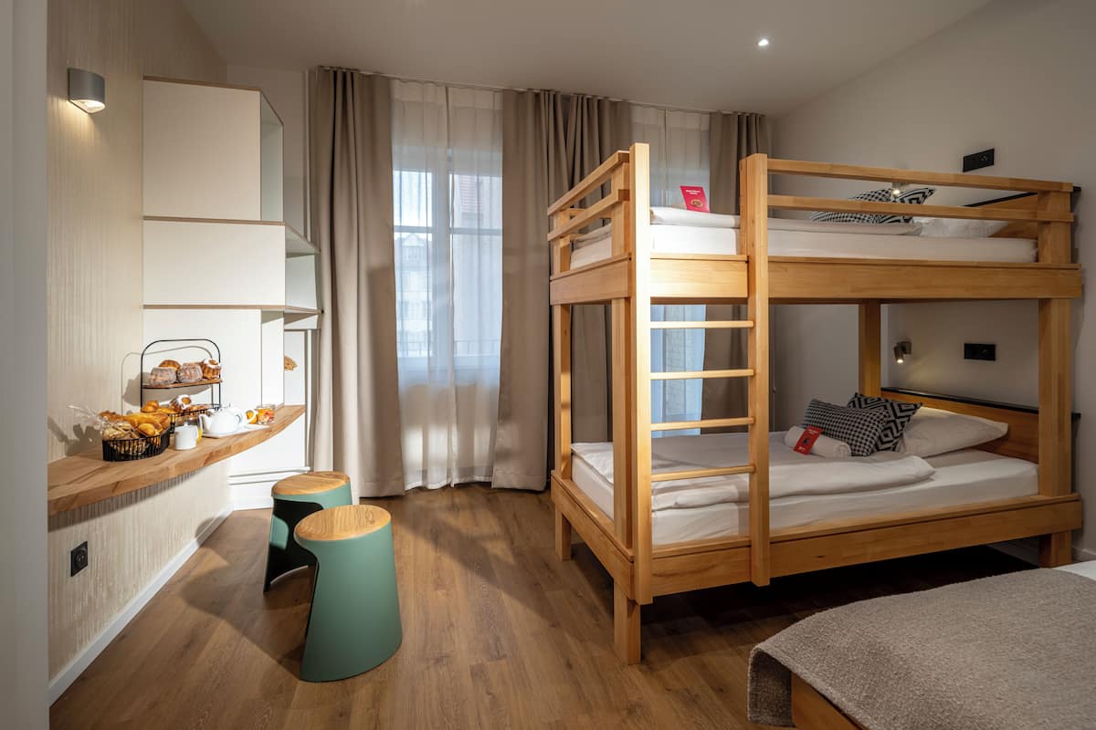 A bunk bed room with a wooden desk, a small stool, and a window with curtains.