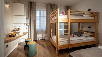 A bunk bed room with a wooden desk, a small stool, and a window with curtains.