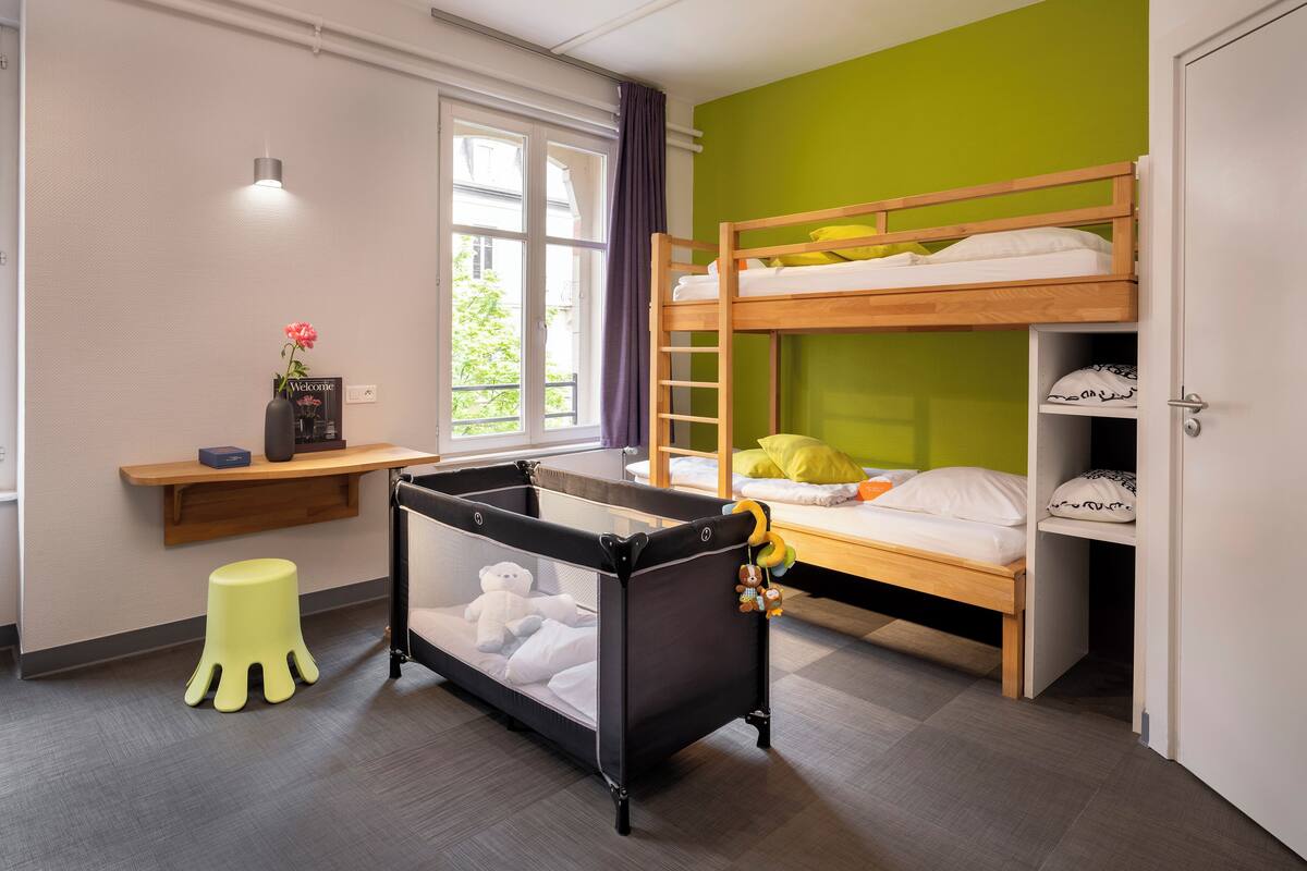 A room with a bunk bed, a desk with a vase, and a small stool.