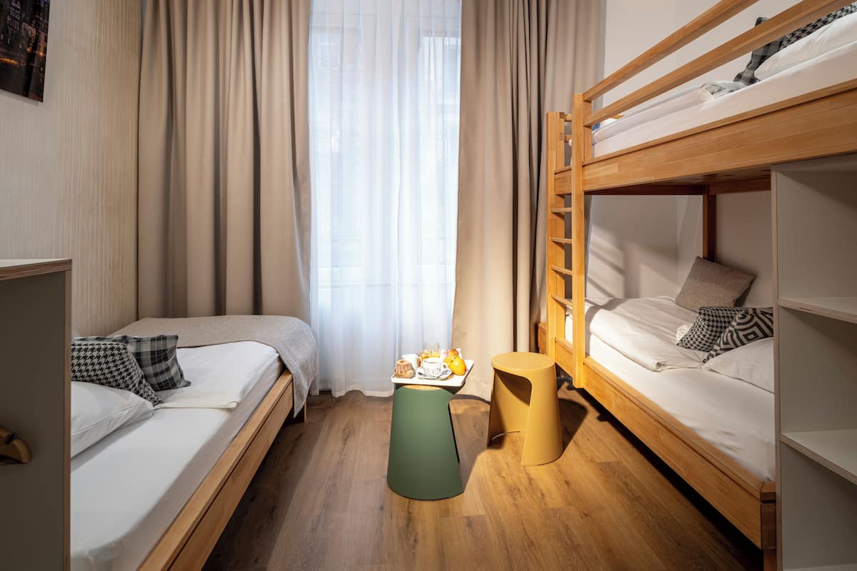 A dormitory room with two single beds, a bunk bed, a small stool, and a breakfast tray on the floor.