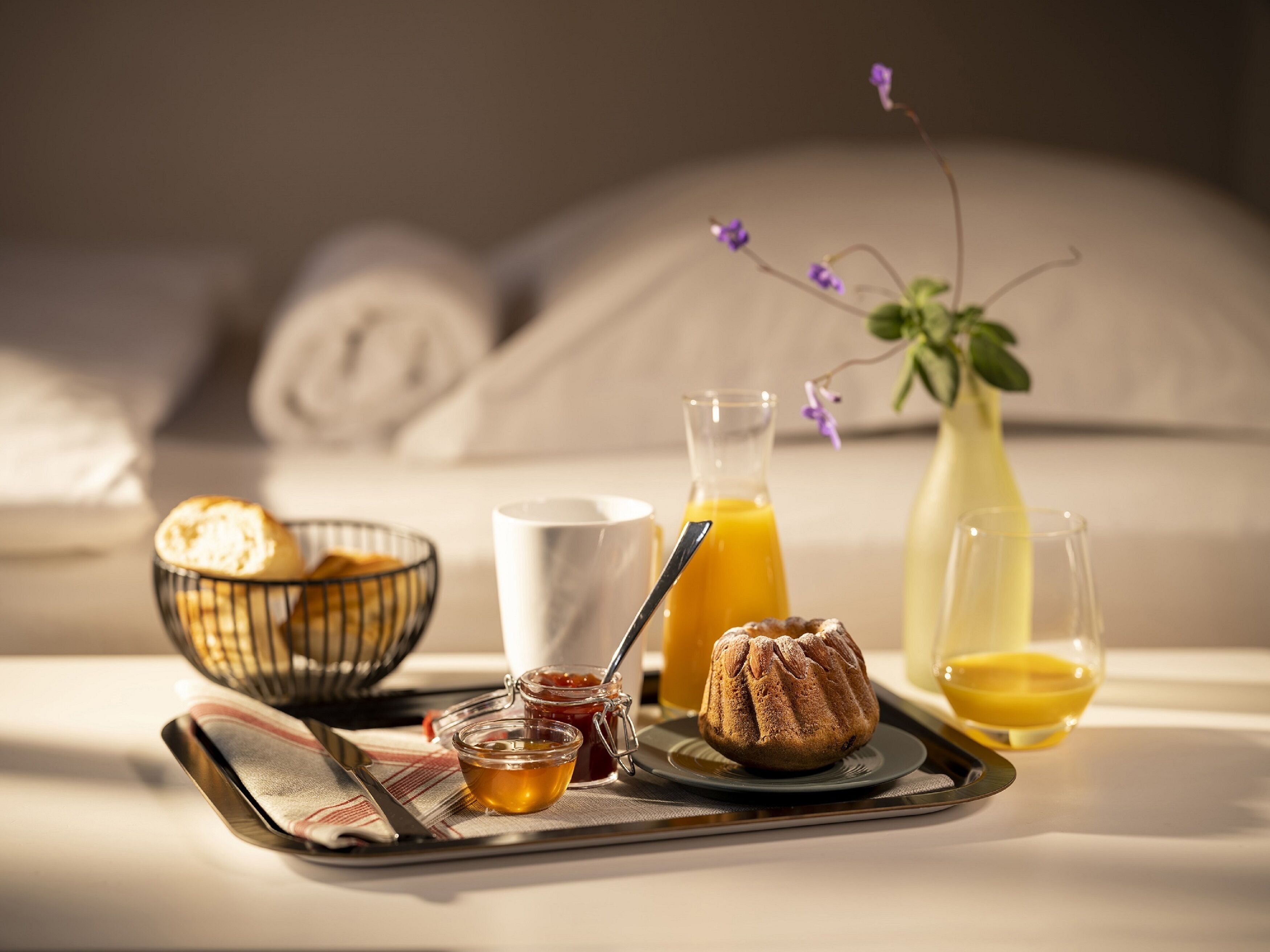 Bandeja de desayuno con pan, un muffin, miel, jugo de naranja y un vaso de leche sobre una cama.