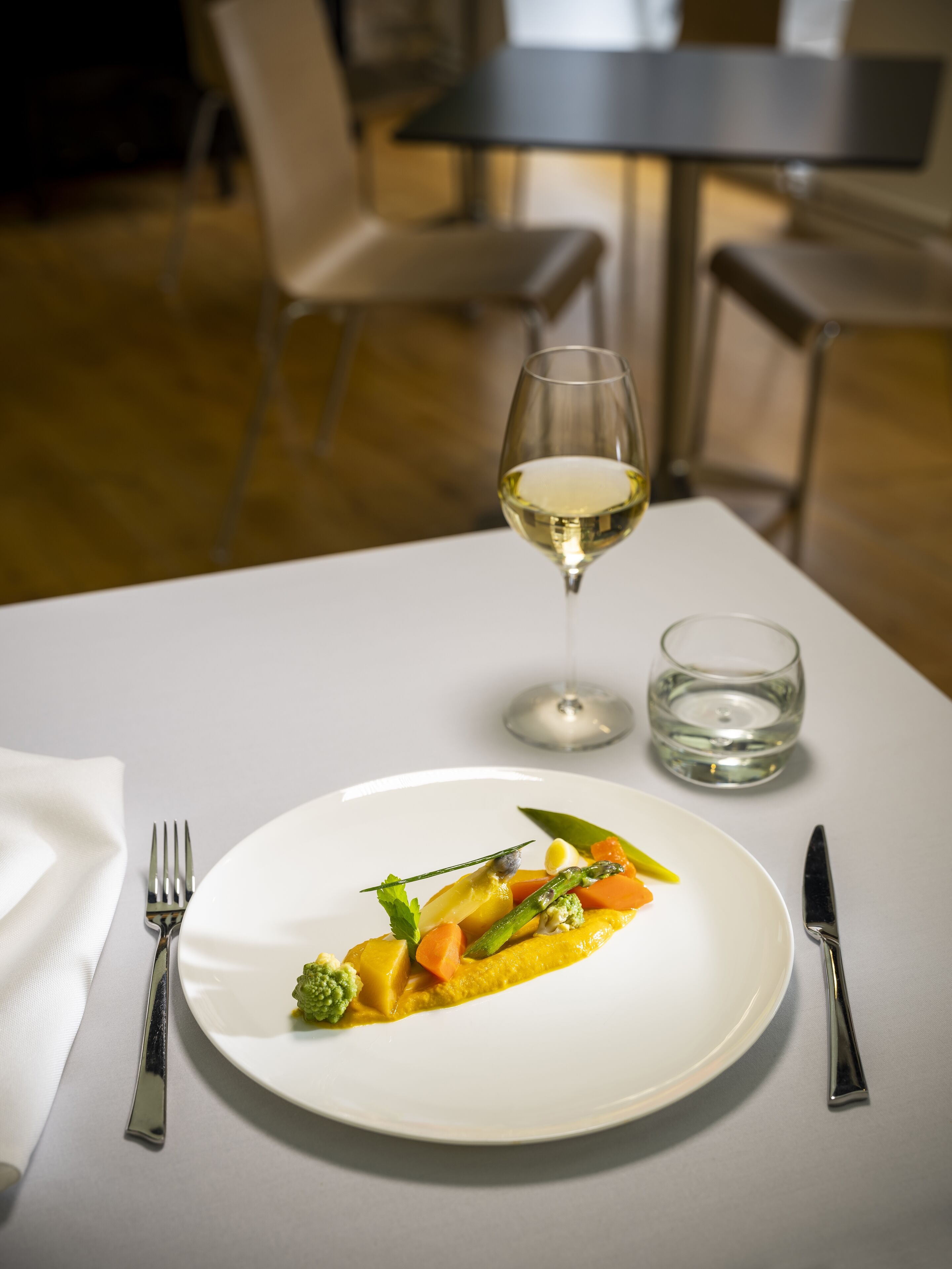 Una mesa de comedor con un plato de comida blanca, una copa de vino blanco y un vaso de agua.