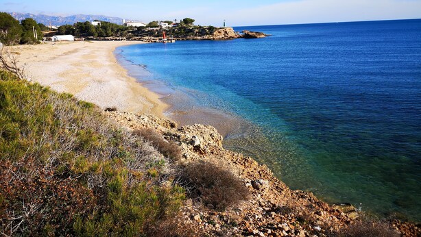 A coastal landscape with a sandy beach, clear blue waters, rocky terrain, and distant buildings. - Nice house for 8 people with private pool, wifi and 400m from the sea. (Ametlla de mar)