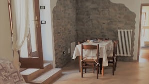Ein Zimmer mit Stehwänden, einem Esstisch mit Stühlen, einer Couch und einem Heizkörper.