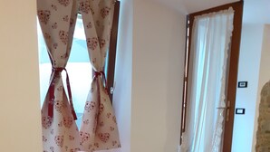 Ein Zimmer mit einer roten Couch, zwei braunen Kissen, einem Fenster mit blumigen Vorhängen und einer Tür mit weißen Vorhängen.
