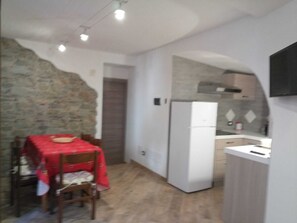 A compact kitchen with a refrigerator, a dining table with chairs, and a stone wall.