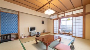 A traditional Japanese room with tatami flooring, a low table, a television, and sliding doors. - Hotel Shiiya (Sado)