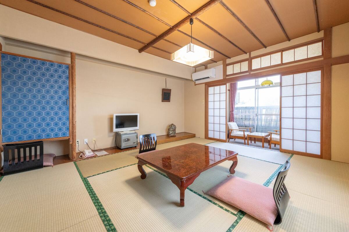 A traditional Japanese room with tatami flooring, a low table, a television, and sliding doors.