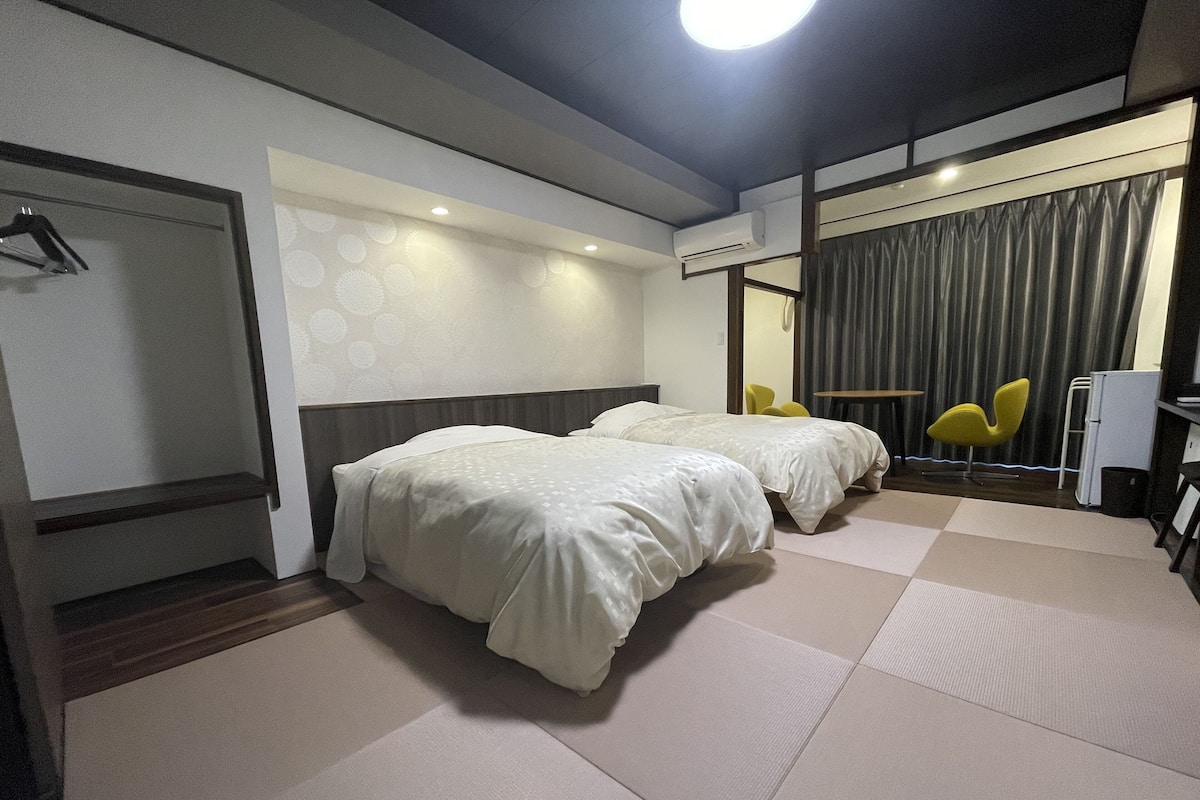 A hotel room with two beds, a desk, a chair, and an air conditioning unit.