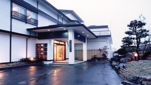 A modern building with a covered entrance, large windows, and a well-maintained garden area. - Hotel Shiiya (Sado)