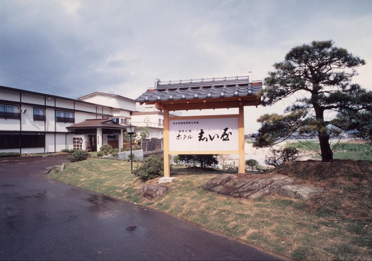 A hotel entrance with a traditional Japanese-style sign, a covered walkway, and a pine tree.