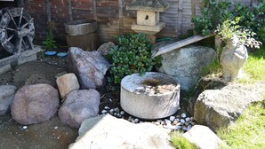 A garden with a stone lantern, large rocks, and a wooden water wheel. - Hotel Shiiya (Sado)