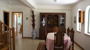 Un comedor con una mesa de madera dispuesta para cuatro personas, un aparador grande con puertas de vidrio y un jarrón alto.