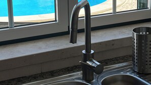 Una cocina con un lavamanos de acero inoxidable y una ventana con vistas a una piscina.