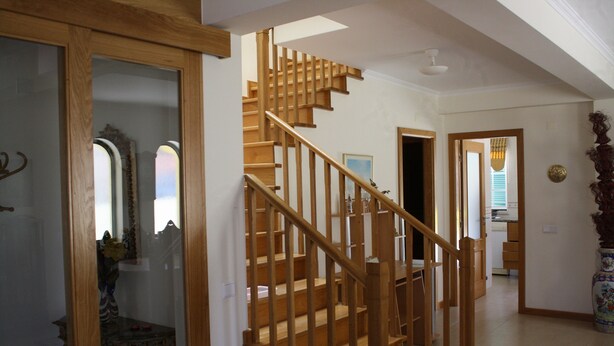 Una escalera de madera con barandilla que conduce a un rellano en el segundo piso. Se ve un espejo y un jarr ón decorativo en el rellano.