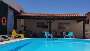 Una piscina con borde de baldosas, un flotador salvavidas y varias sillas de plástico.