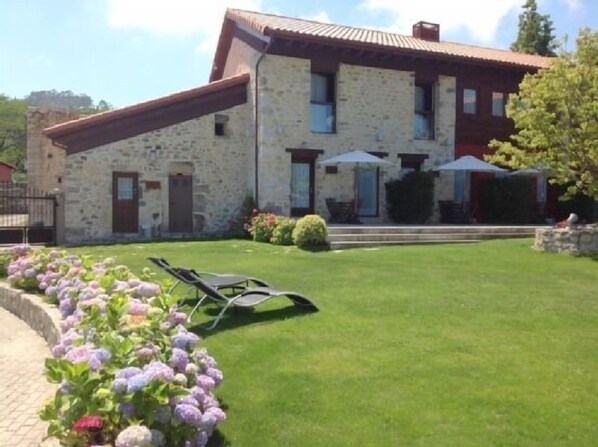 A stone building with a red roof, a small garden with flowers, and a lawn.