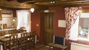 Un coin repas accueillant avec une table et des chaises en bois, un téléviseur posé sur un petit meuble et une fenêtre agrémentée de rideaux.