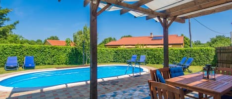 A pool area with a covered patio, lounge chairs, and a table.