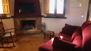 Ein Wohnzimmer mit Kamin, einem darüber montierten Fernseher, einem roten Sofa und einem hölzernen Schaukelstuhl.