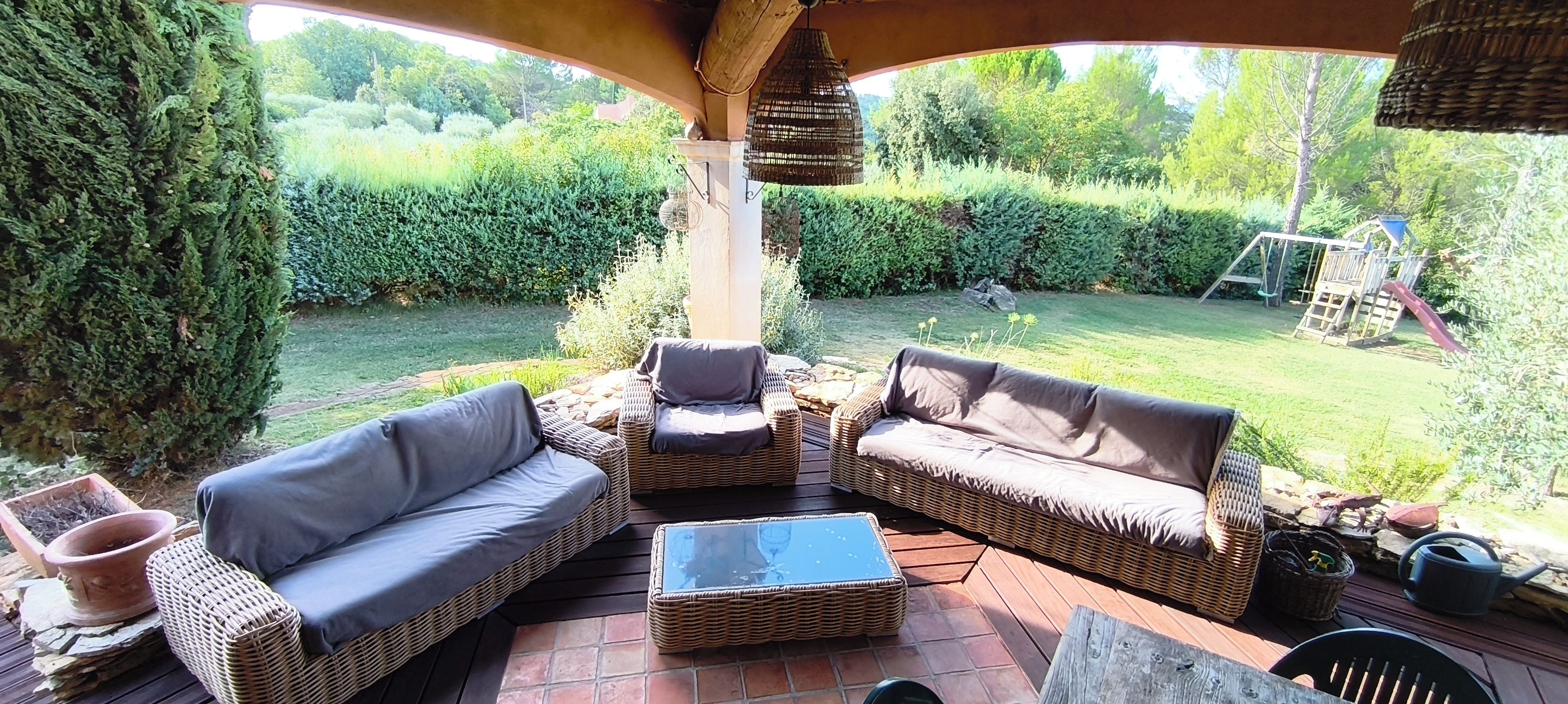 An outdoor patio with wicker furniture, a stone table, and a view of a garden.