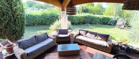 An outdoor patio with wicker furniture, a stone table, and a view of a garden.