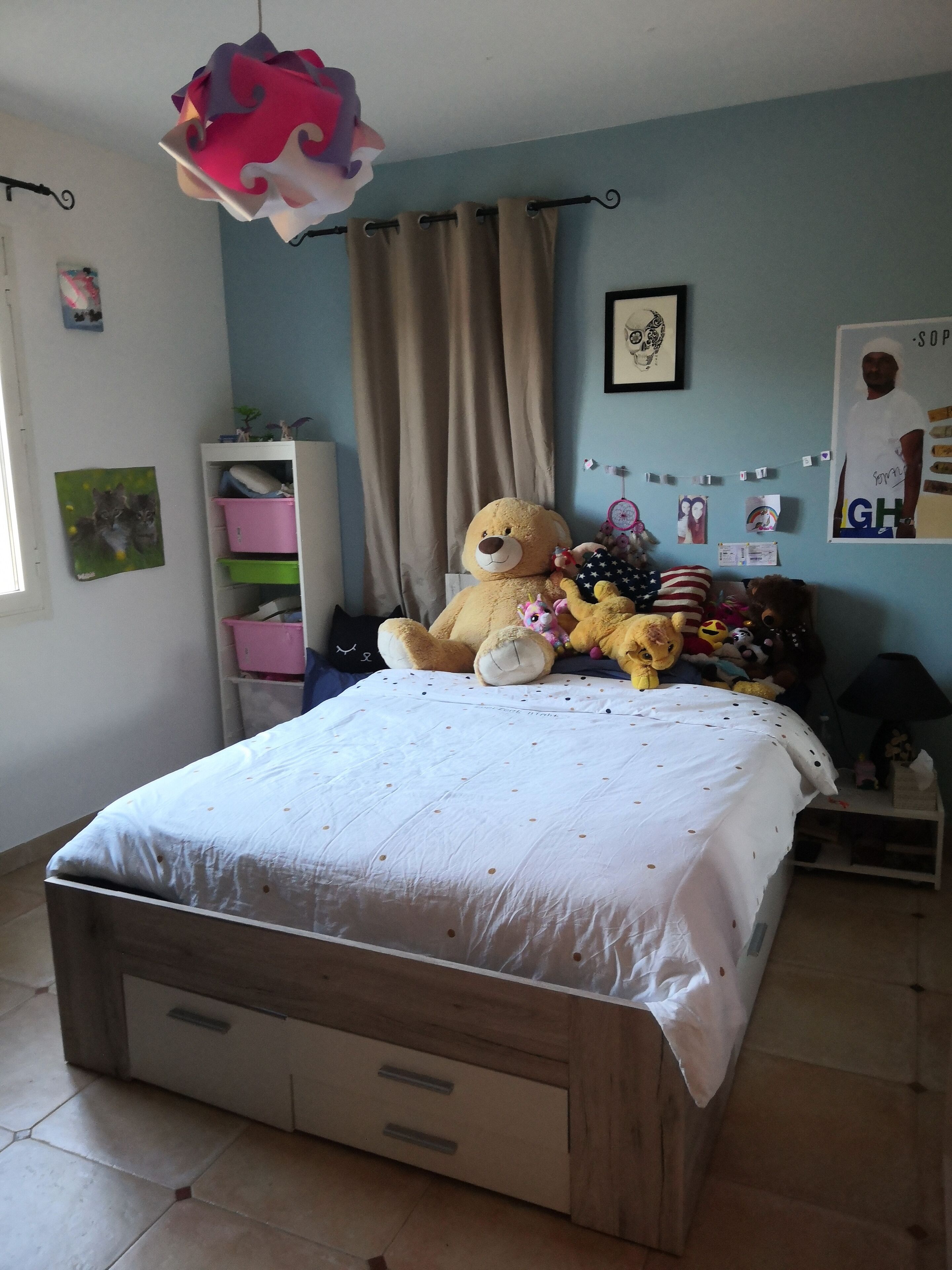 Un dormitorio con una cama grande, un armario, una cómoda, una lámpara colgante y una pared con varios adornos.
