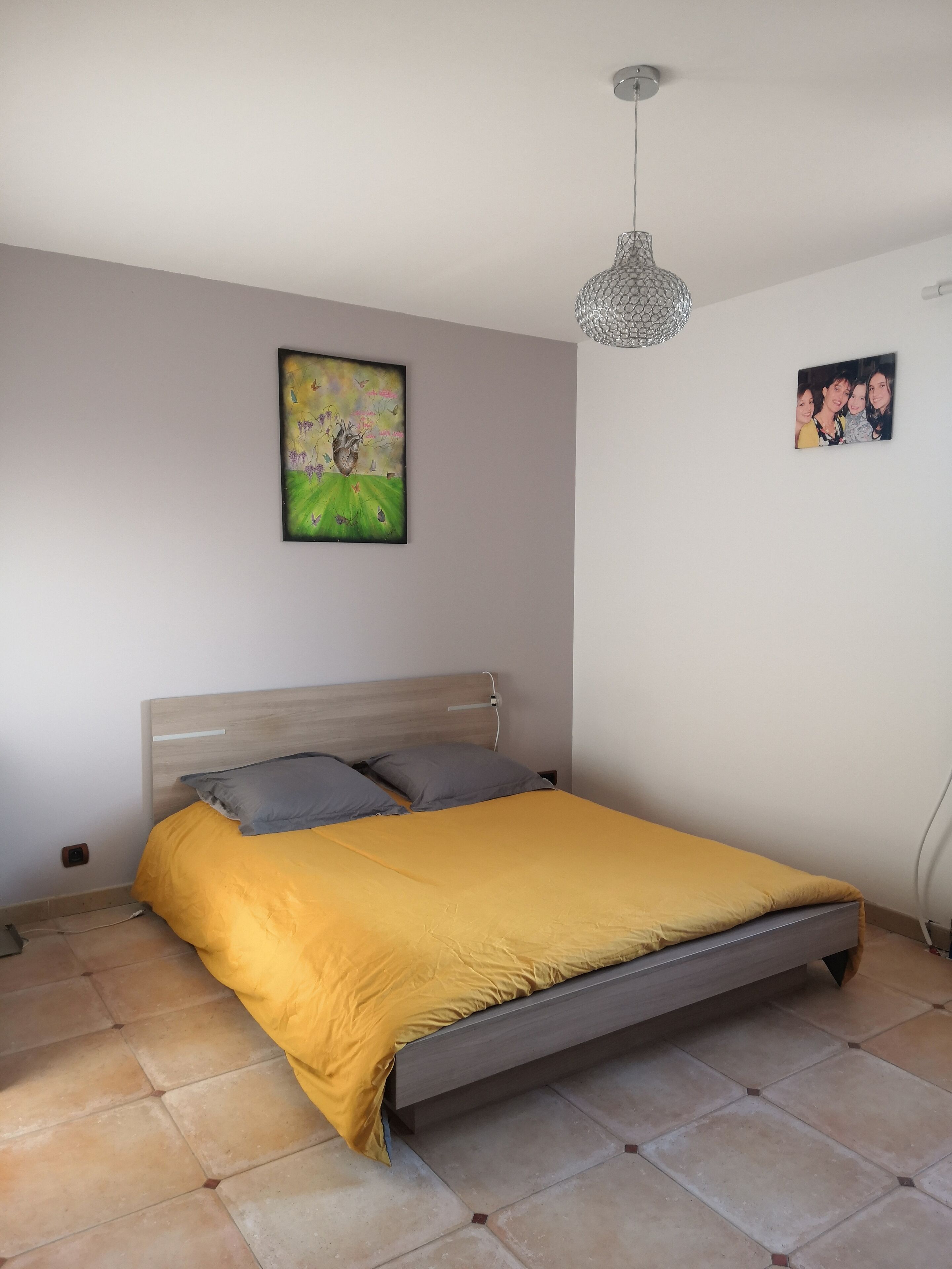 Une chambre à coucher comprenant un lit, une tête de lit, un tableau accroché au mur et un luminaire fixé au plafond.