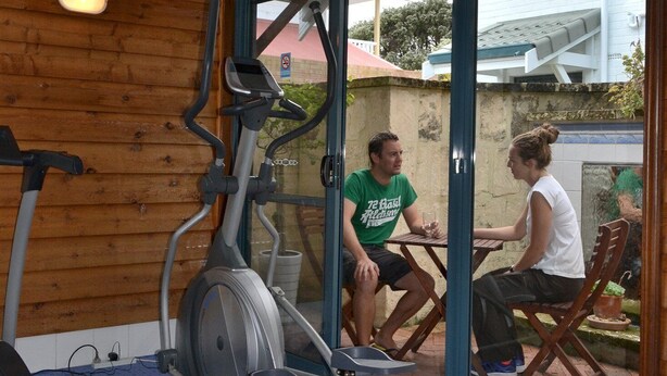 A gym with exercise equipment, wooden walls, and a glass door leading outside. - SELF CONTAINED-2 Bdrm Apartments (Albany)