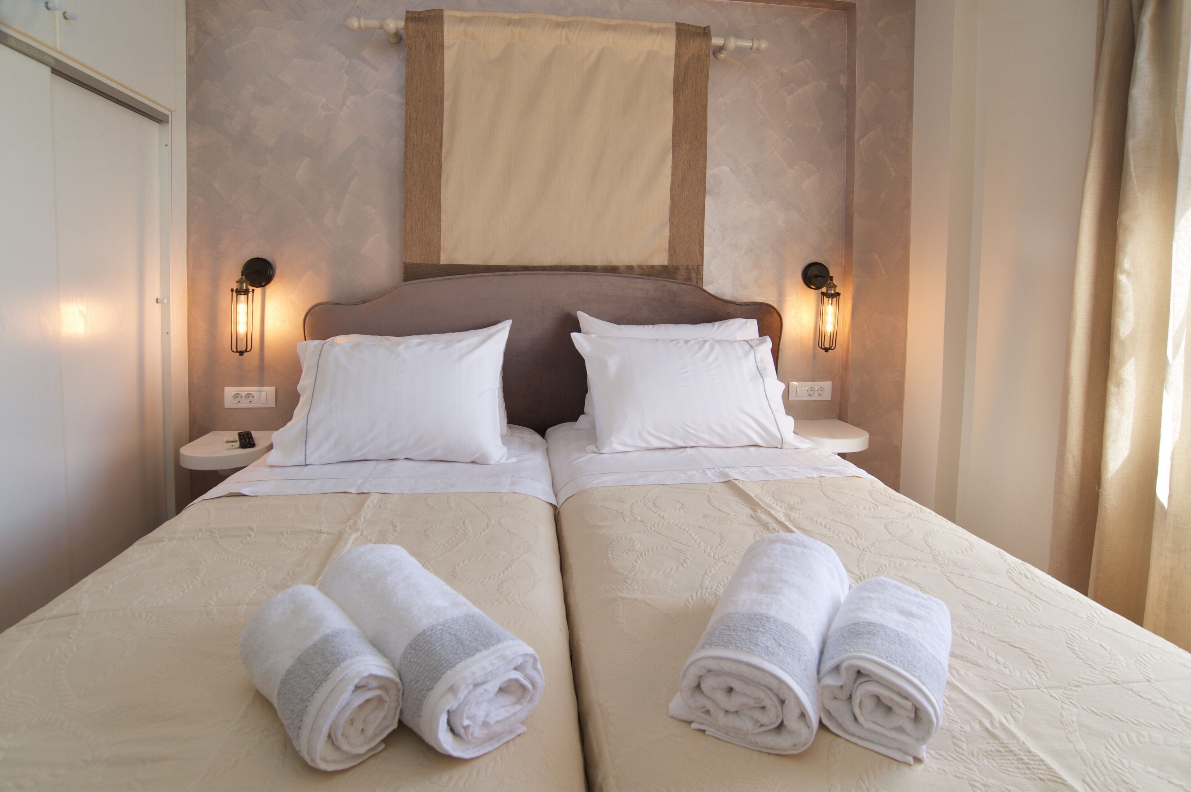 Cama doble con dos almohadas, mesita de noche con lámpara y toallas enrolladas sobre la cama.