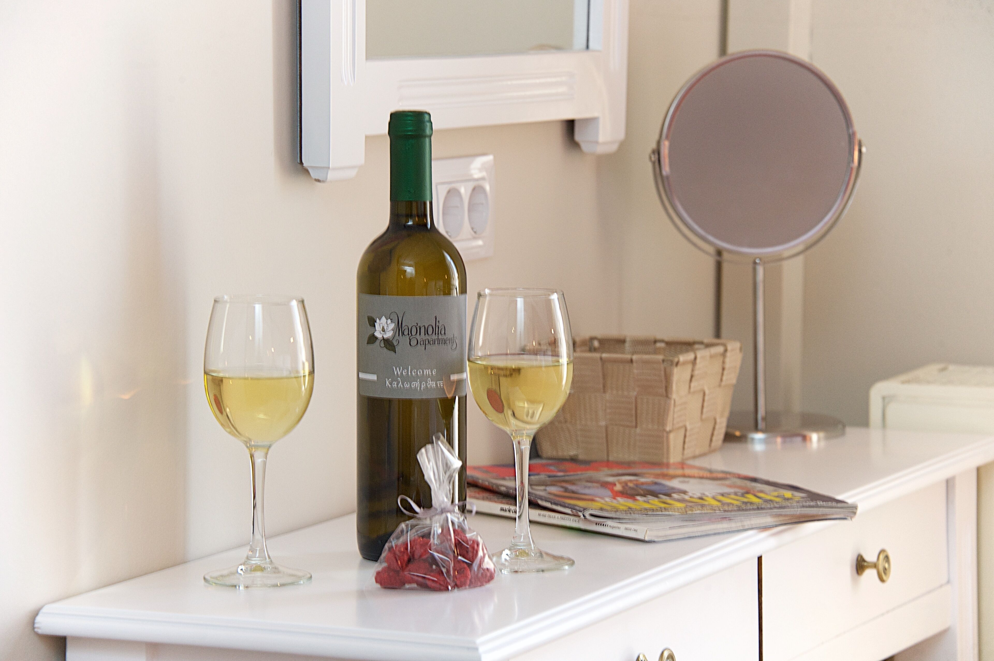 A bottle of wine, two glasses, and a small bag of snacks on a white table.
