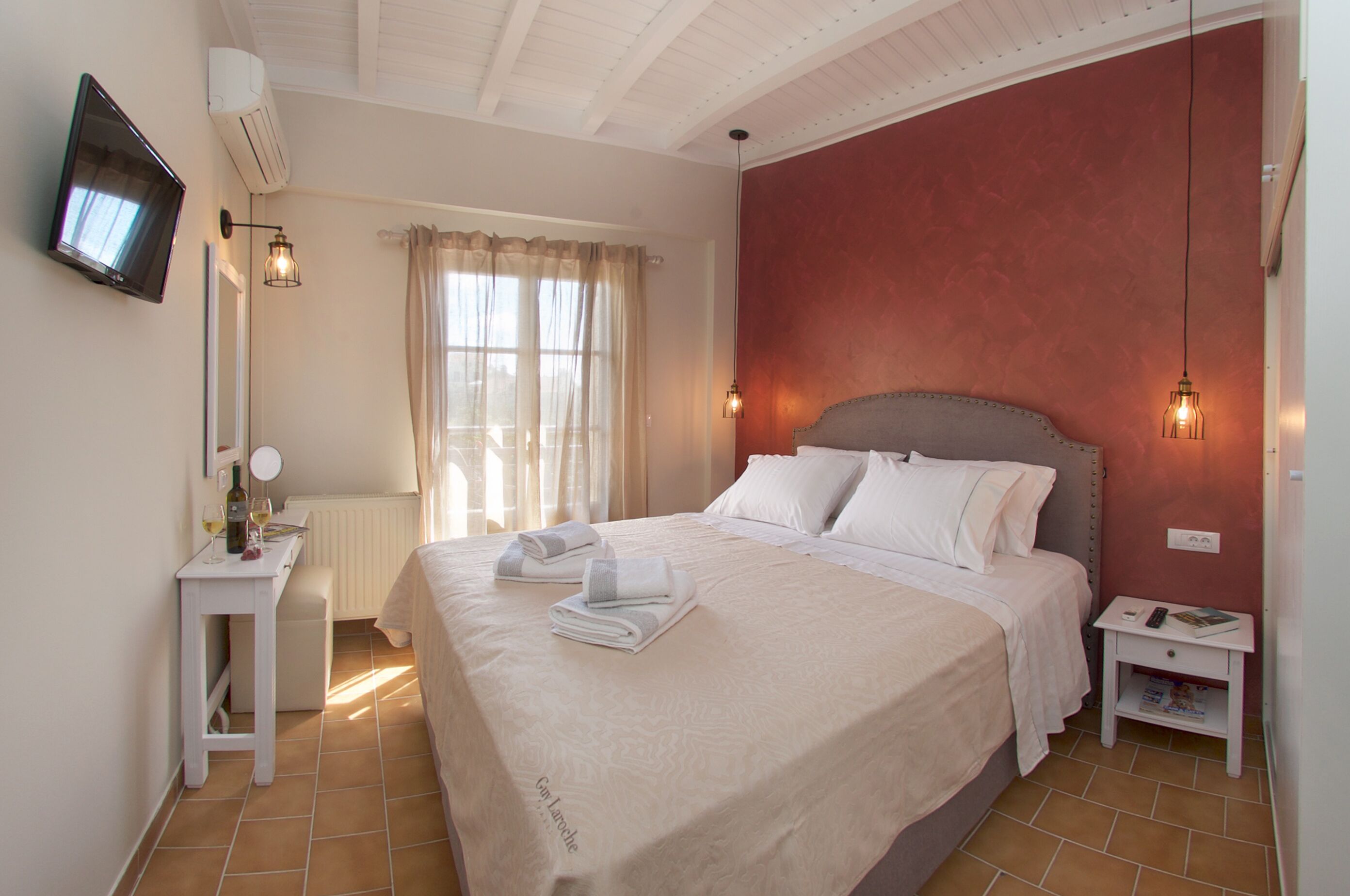 A neatly made bed with white linens, a bedside table with a remote control, and a wall-mounted TV.