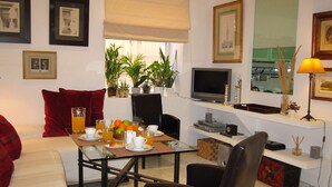 Un comedor con una mesa lista para dos personas, un televisor y una ventana con plantas.