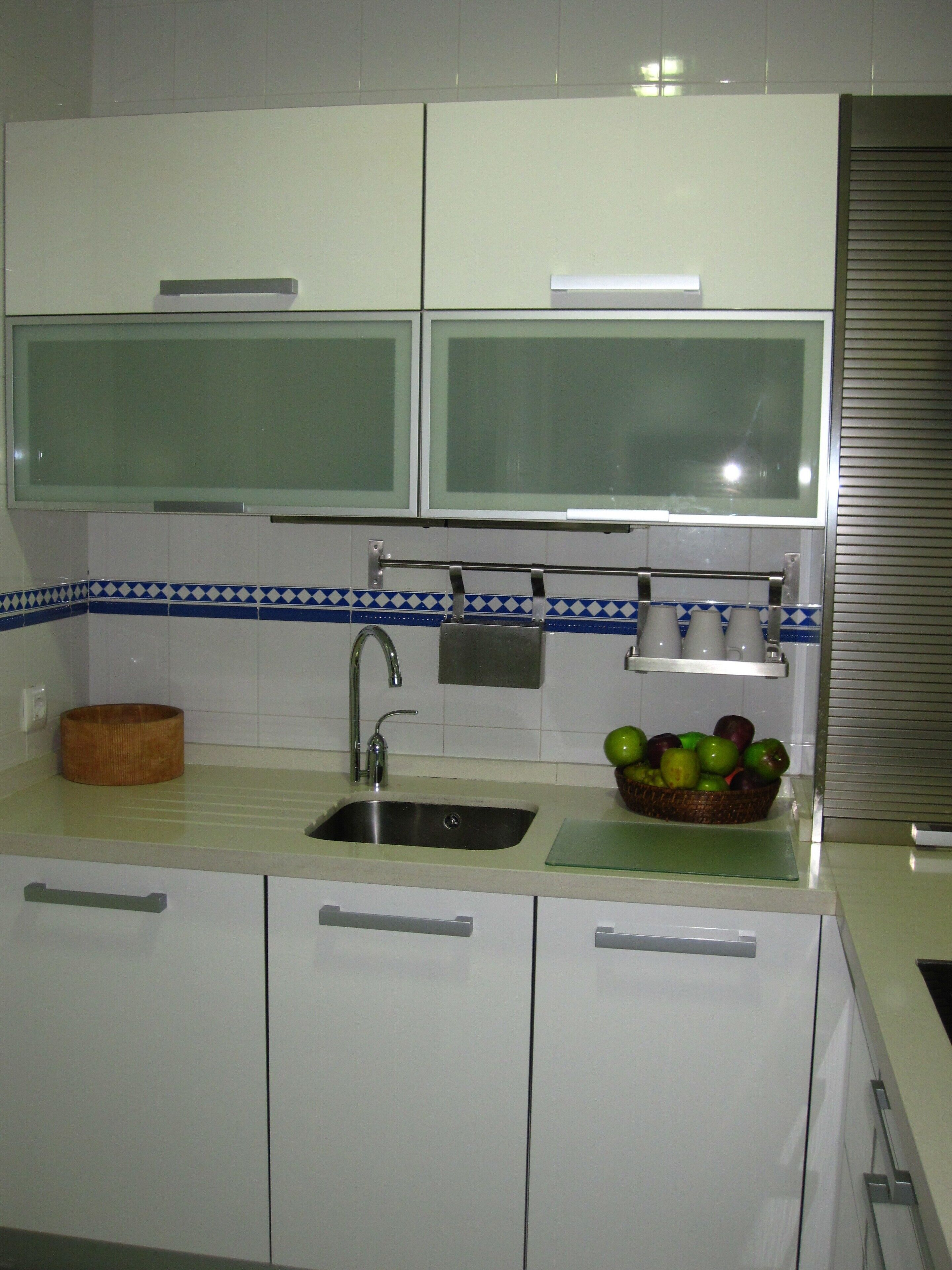 Una cocina con armarios blancos, un lavamanos de acero inoxidable y una cesta de frutas sobre la encimera.