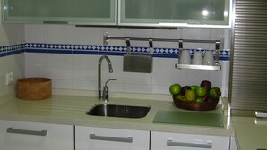 Una cocina con armarios blancos, un lavamanos de acero inoxidable y una cesta de frutas sobre la encimera.