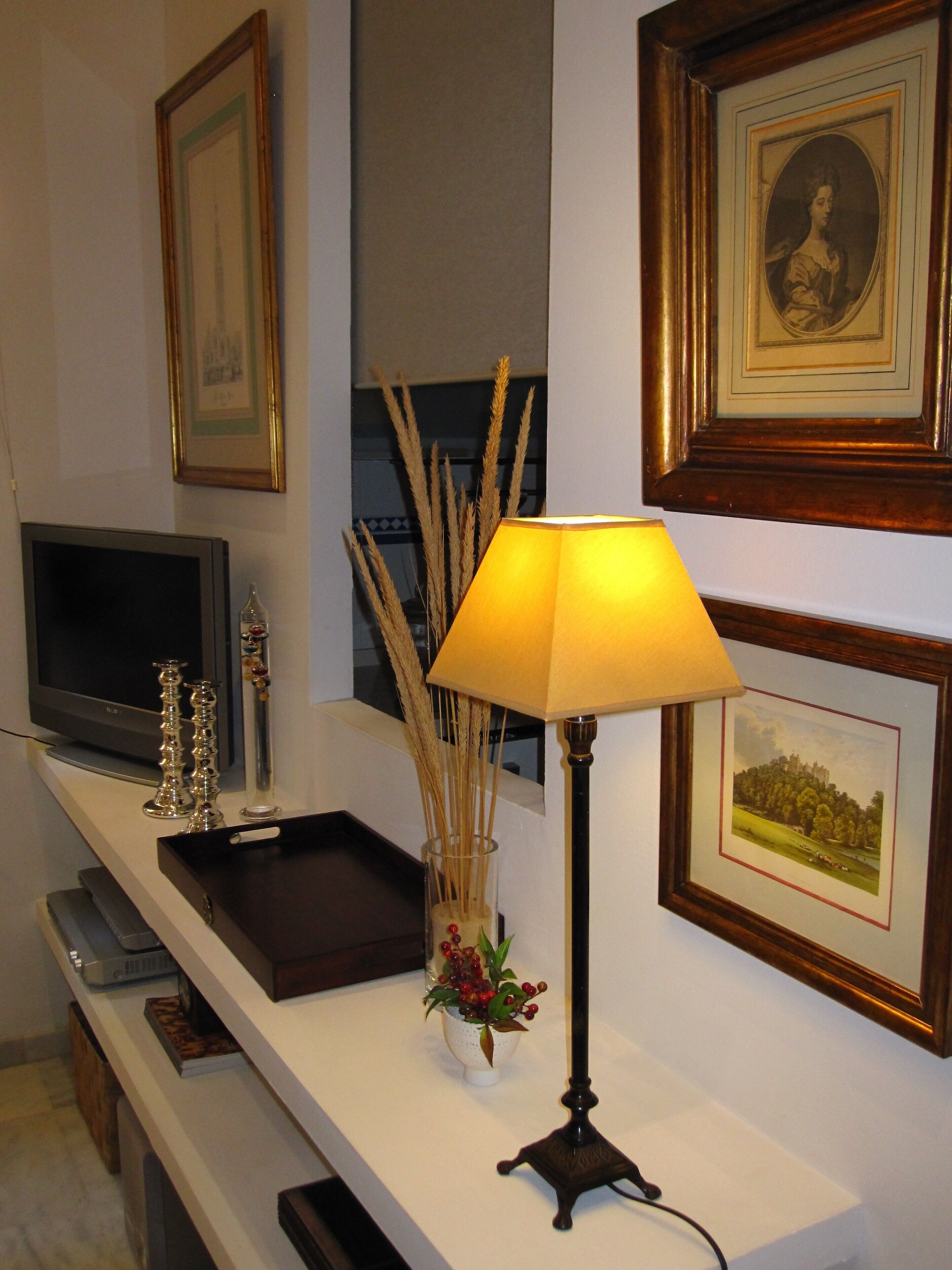 Een kamer met een flatscreen televisie, een lamp, een dienblad en afbeeldingen in lijsten aan de muur.