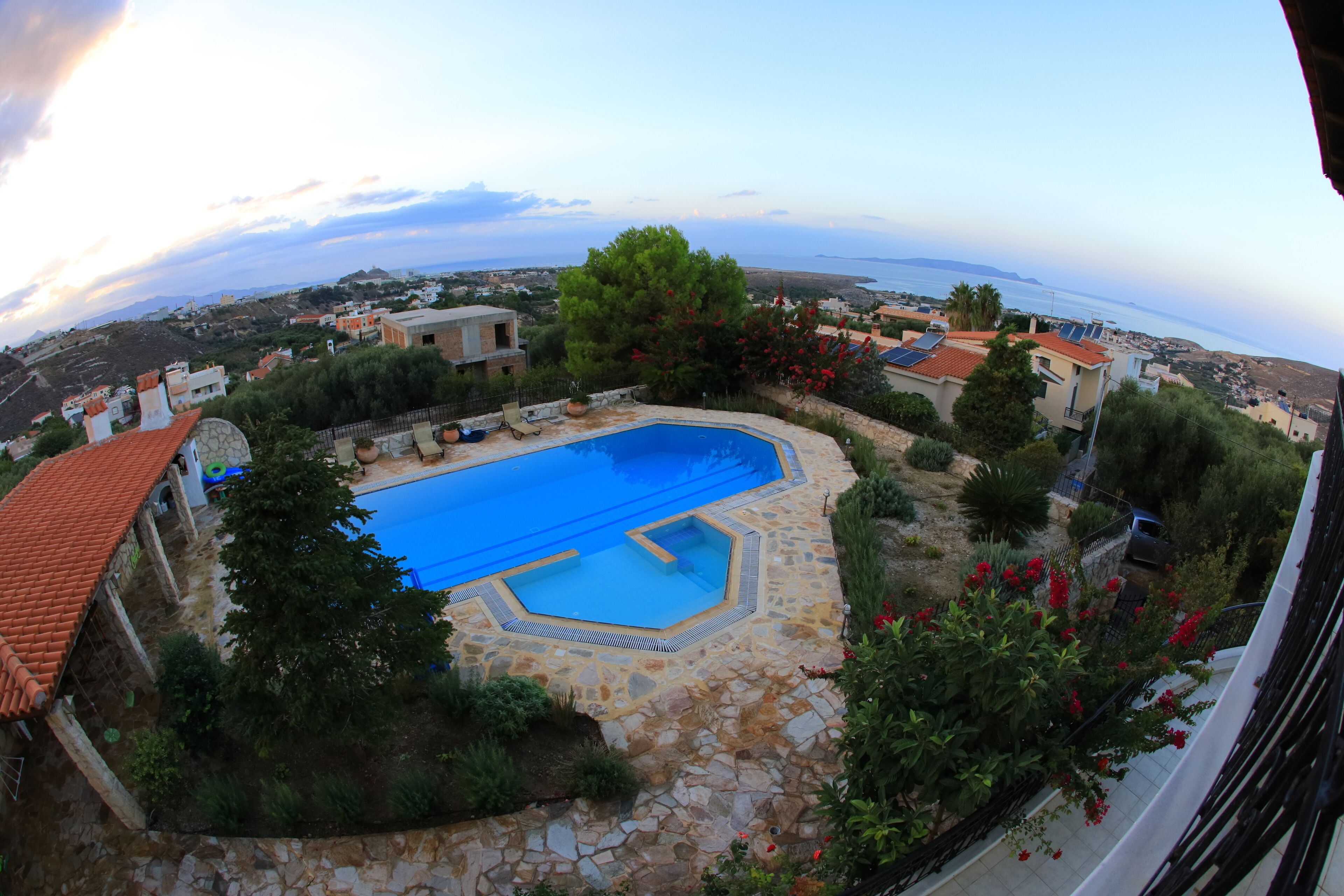 A pool surrounded by stone tiles, with a view of the sea and distant buildings.