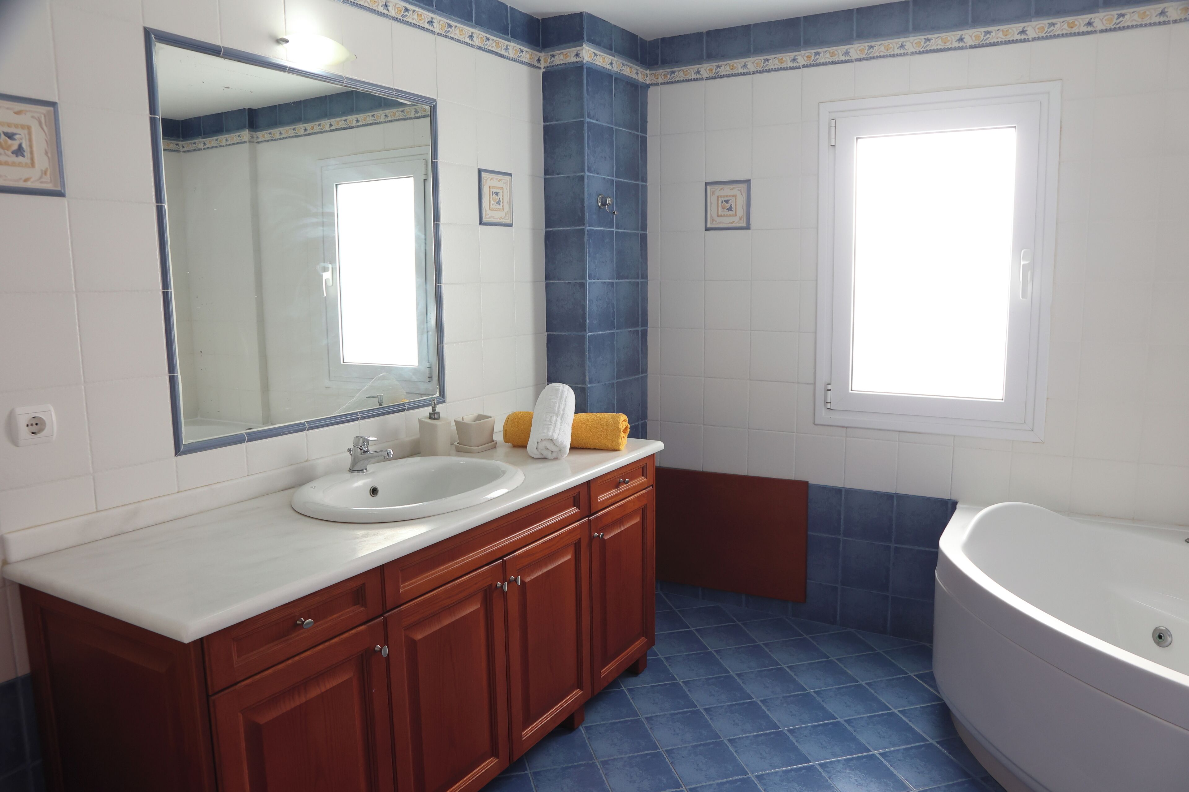Un baño con lavamanos blanco, tocador de madera, un espejo grande y una bañera.