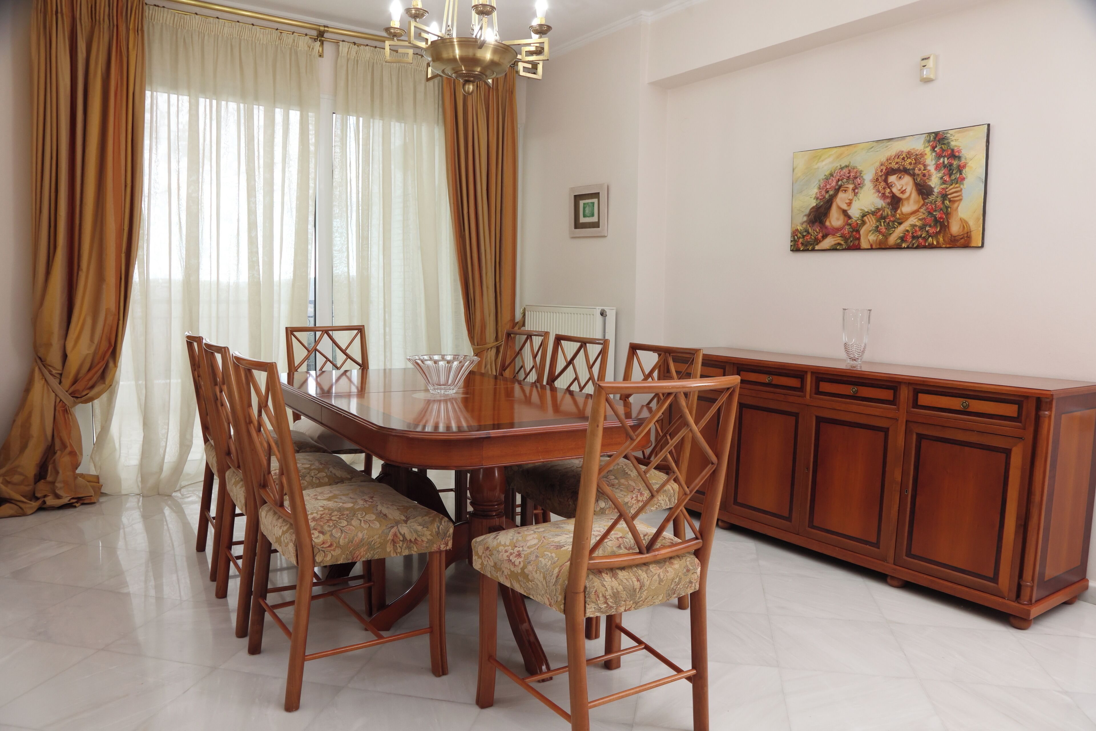 A dining area with a wooden table and chairs, a chandelier, and a painting on the wall.