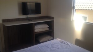 Ein Schlafzimmer mit einem Bett, einem an der Wand befestigten Fernseher und einem Fenster.