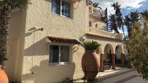 A two-story building with a stucco exterior, large windows, and a balcony with railings. There are potted plants and a tiled roof. - Marbella Villa on the beach (Marbella)