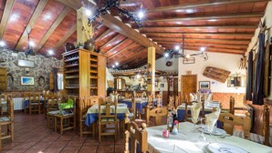 A rustic dining area with wooden tables and chairs, stone walls, and a tiled floor.