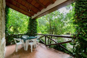 Une terrasse extérieure avec une table et des chaises, entourée d’une végétation luxuriante et d’une clôture en bois.